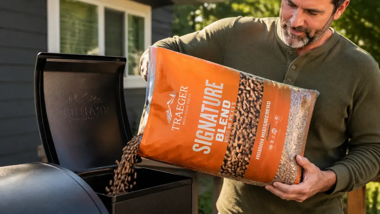 Hand pouring Traeger Signature Blend wood pellets into a pellet grill hopper